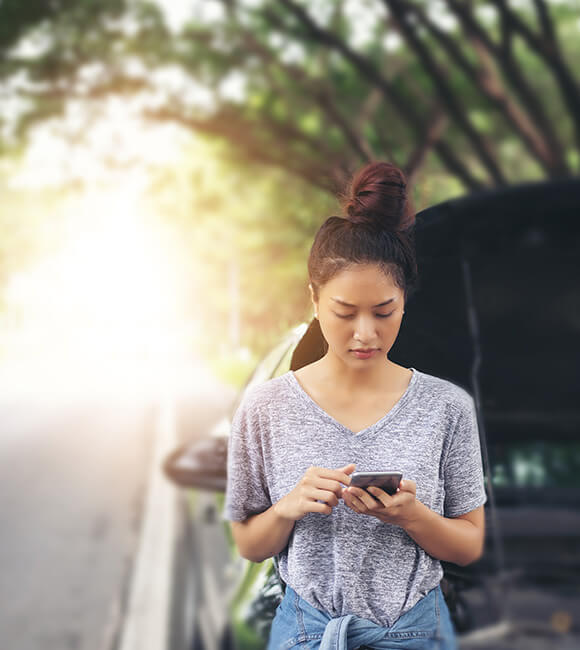 woman dialing phone in front of broken down car